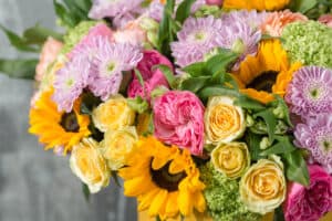 beautiful bouquet of mixed flowers in a vase on wooden table. the work of the florist at a flower shop. a bright mix of sunflowers, chrysanthemums and roses